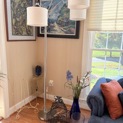 Sale Photo Thumbnail #135: Modern brushed metal multi-arm arc floor lamp with off-white drum shades, positioned in a room corner beside framed artwork and decorative home accent pieces.