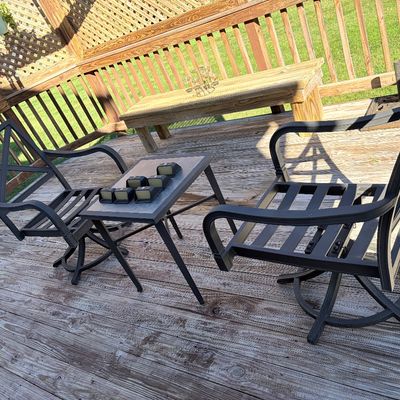 Sale Photo Thumbnail #95: Black metal outdoor patio set including two swivel armchairs and a matching tile-top side table on a wooden deck.