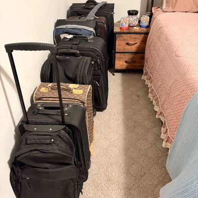 Sale Photo Thumbnail #228: Collection of rolling luggage pieces and travel bags lined up in a bedroom, including soft-sided black suitcases and a pattern-print carry-on.