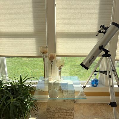 Sale Photo Thumbnail #117: Bushnell reflecting telescope on an adjustable tripod stand positioned next to a post-modern glass-top end table with a textured stone pedestal base.