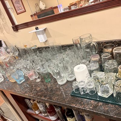 Sale Photo Thumbnail #186: Large collection of assorted glassware, including beer mugs, tumblers, shot glasses, and stemware arranged on a granite bar counter.