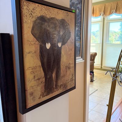 Sale Photo Thumbnail #153: Framed canvas wall art depicting a dark elephant with map text and gold foil accents in a black float frame.