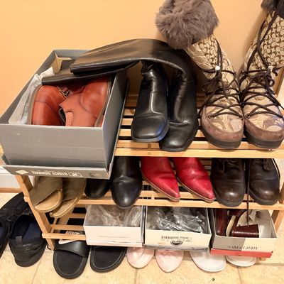Sale Photo Thumbnail #161: Collection of men's and women's footwear arranged on a wooden shoe rack, including Coach pattern fur-trimmed winter boots, leather ankle boots, dress shoes, and casual slides.