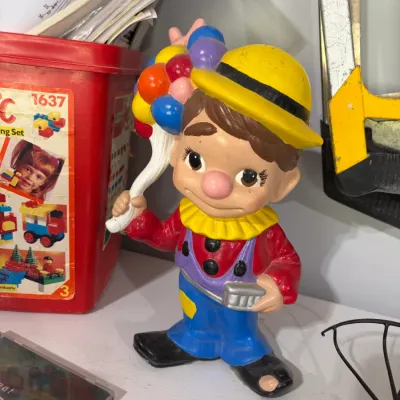 Sale Photo Thumbnail #20: Vintage painted ceramic or plaster clown figurine holding colorful balloons, wearing a yellow hat, red shirt, and blue overalls.