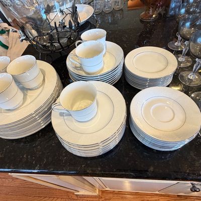Sale Photo Thumbnail #102: Vintage white fine china dinnerware service with silver rim detail, accompanied by stacks of plates, teacups, and smoky glass stemware.