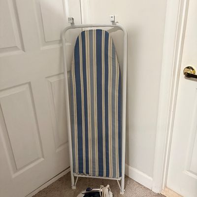 Sale Photo Thumbnail #232: Wall-mounted over-the-door folding ironing board with a blue and cream striped cover, paired with a black steam iron.