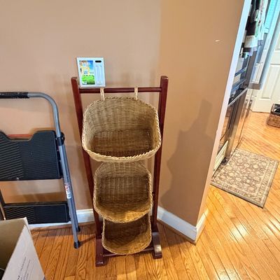 Sale Photo Thumbnail #104: Three-tier woven wicker basket organizer on a dark wood stand alongside a metal step stool.