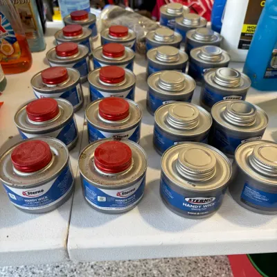 Sale Photo Thumbnail #17: Large collection of Sterno Handy Wick 6-hour chafing fuel cans arranged on a table.