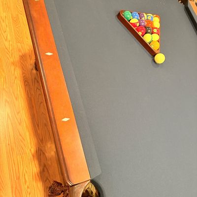 Sale Photo Thumbnail #242: Traditional wood billiard table with blue felt, leather fringe drop pockets, diamond sights, and a set of pool balls in a wooden rack.