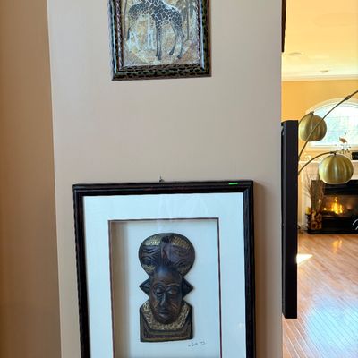 Sale Photo Thumbnail #154: Framed African safari wall art featuring a leopard-pattern framed giraffe print and a shadow box framed carved wooden African mask signed and dated 1999.