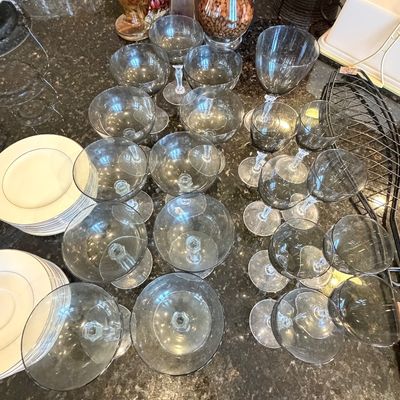 Sale Photo Thumbnail #101: Collection of smokey black tinted glassware including coupe glasses and wine stems, displayed on a granite countertop alongside china plates.