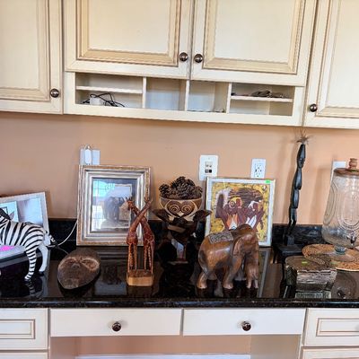 Sale Photo Thumbnail #155: Collection of safari-themed decor including hand-carved wooden elephant and giraffe figurines, framed African art prints, a zebra figure, and a glass beverage dispenser arranged on a countertop.
