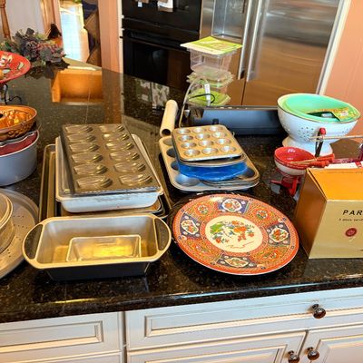Sale Photo Thumbnail #90: Assorted bakeware and kitchenware displayed on a granite countertop, including a copper Bundt pan, Madeleine tins, loaf pans, and a decorative Asian-style serving platter.
