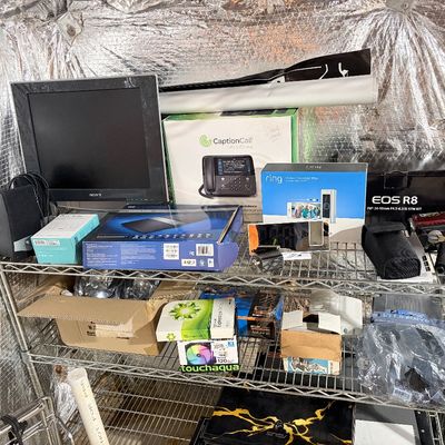 Sale Photo Thumbnail #202: Collection of mixed electronics and computer accessories, including a Sony monitor, Ring Doorbell Pro box, Canon EOS R8 kit box, and various components displayed on wire shelving.