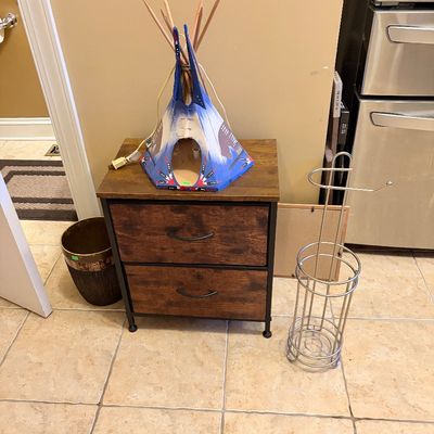 Sale Photo Thumbnail #158: Novelty teepee-shaped table lamp resting on a modern two-drawer rustic brown nightstand, accompanied by a freestanding chrome toilet paper holder.