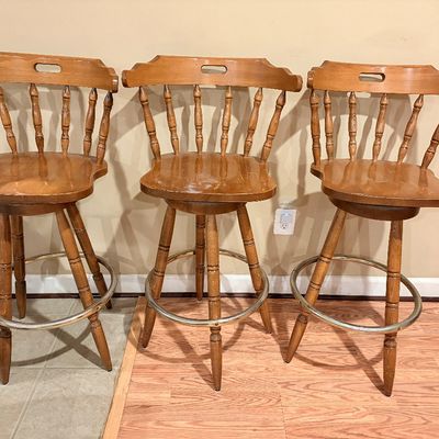 Sale Photo Thumbnail #254: Set of three vintage wooden swivel barstools featuring spindle backs, contoured seats, and circular brass footrests.