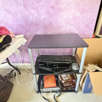 Sale Photo Thumbnail #296: Three-tiered black media cart with silver legs, holding electronics including a keyboard and calculator on the middle shelf and a small hard case on the bottom shelf.