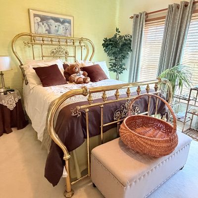 Sale Photo Thumbnail #295: Vintage brass bed frame with ornate spindle detailing, dressed with bedding and accent pillows, paired with an upholstered storage bench and a woven wicker basket at the foot.