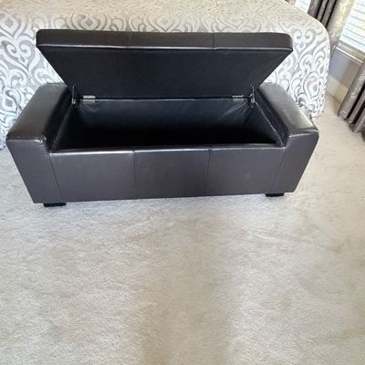 Sale Photo Thumbnail #308: Dark brown faux leather storage ottoman bench with an open hinged lid, positioned at the foot of a bed.