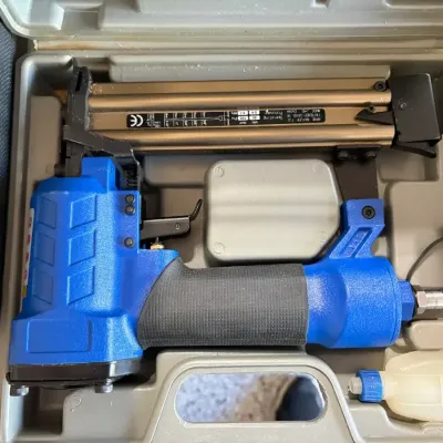 Sale Photo Thumbnail #29: Blue 18-gauge pneumatic brad nailer in a molded plastic storage case, complete with oil bottle accessory.