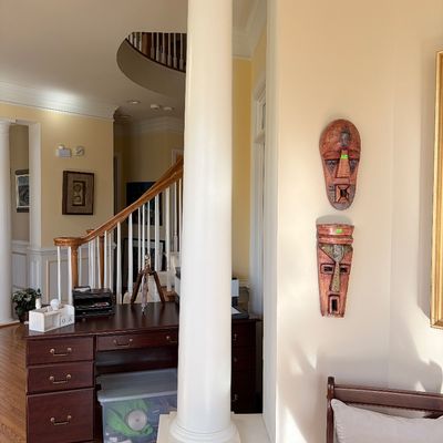 Sale Photo Thumbnail #130: Pair of carved African-style decorative wall masks mounted near a dark wood executive desk and architectural column in a entryway.