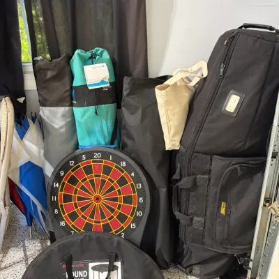 Sale Photo Thumbnail #76: Collection of outdoor recreation gear including a soft golf travel bag, folding camp chairs in carrying cases, a portable round table in a case, and an electronic dartboard.