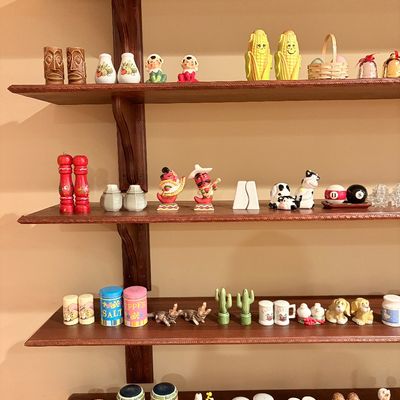 Sale Photo Thumbnail #182: Collection of vintage ceramic and novelty salt and pepper shakers displayed on dark wood shelving, including tiki, chili pepper, and animal designs.