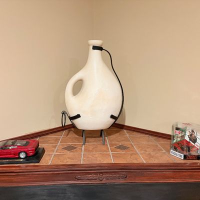 Sale Photo Thumbnail #252: Large off-white ceramic jug on a black metal stand, flanked by a red Jaguar model car and a packaged Scarface puzzle cube.