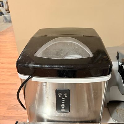 Sale Photo Thumbnail #238: Countertop portable ice maker with a stainless steel body and black trim lid. Features a front control panel for ice size selections and indicator lights.