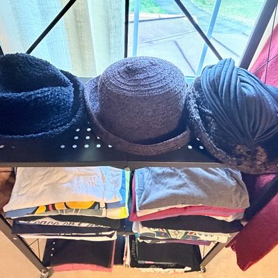 Sale Photo Thumbnail #268: Trio of vintage women's textured hats, including bouclé and faux fur styles, displayed on a black metal shelf above folded clothing.