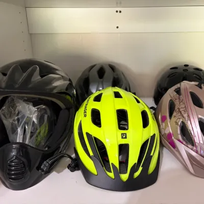Sale Photo Thumbnail #42: Assortment of modern bicycle helmets on a shelf, including a high-visibility yellow Bontrager helmet, a patterned Bell helmet, and a black full-face helmet.