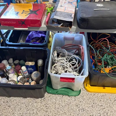 Sale Photo Thumbnail #77: Assorted workshop items, including spray paint cans, power cords, and TV wall mount hardware organized in plastic storage totes and on a folding table.