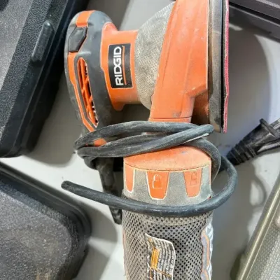 Sale Photo Thumbnail #30: Ridgid electric random orbit sander with attached dust collection bag and power cord wrapped around the handle.