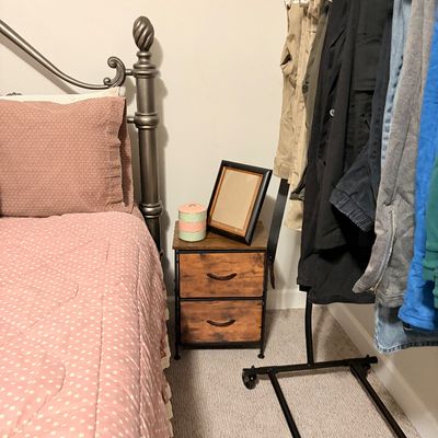Sale Photo Thumbnail #229: Rustic industrial nightstand with two fabric drawers and a black metal frame, positioned between a bed and a rolling clothing rack.