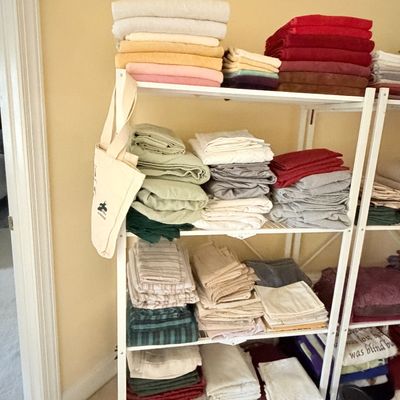 Sale Photo Thumbnail #273: White wire shelving unit filled with neatly folded bed linens, bath towels, and blankets in various colors.