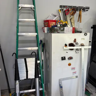 Sale Photo Thumbnail #23: Tall green fiberglass stepladder standing next to a white refrigerator, a collapsible aluminum ladder, and various hand tools and rulers.