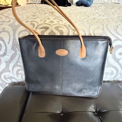Sale Photo Thumbnail #305: Black leather tote bag with tan handles and central emblem patch, featuring a zip-top closure.