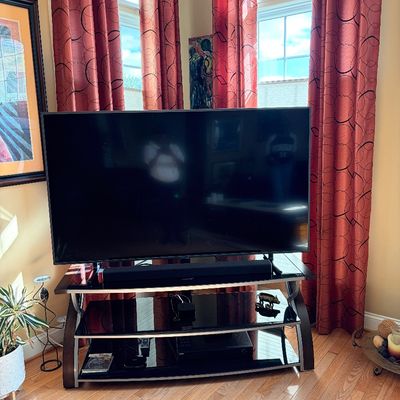 Sale Photo Thumbnail #213: Large flat-screen television with a soundbar, displayed on a modern three-tier glass and metal media stand.