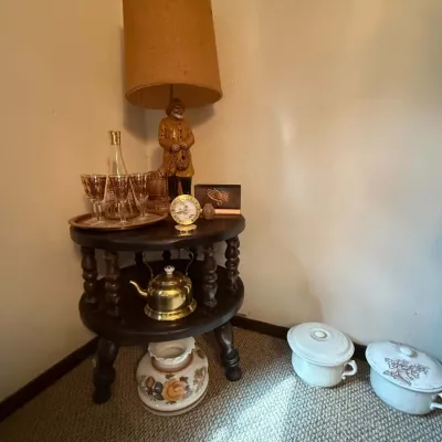 Sale Photo Thumbnail #41: Vintage dark wood two-tiered spindle side table display featuring a figurative table lamp, amber glassware set, small brass kettle, and ceramic chamber pots.
