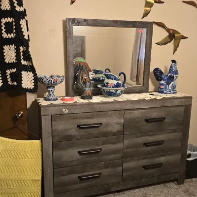 Sale Photo Thumbnail #21: Modern weathered grey six-drawer dresser with attached matching rectangular mirror, topped with blue and white ceramics and decorative figurines.