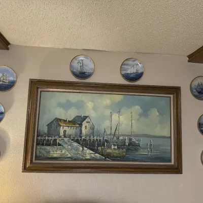 Sale Photo Thumbnail #53: Large framed oil painting depicting a coastal harbor scene, surrounded by a set of eight decorative maritime collector plates.