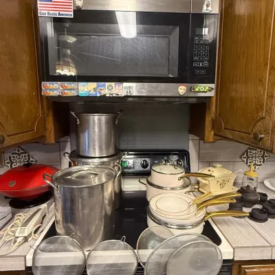 Sale Photo Thumbnail #33: An assortment of kitchenware set on a stove top, including large stainless steel stock pots, a vintage enamel cookware set with brass-tone handles, and mesh splatter screens.