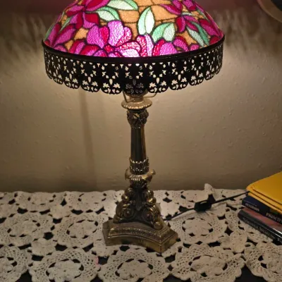 Sale Photo Thumbnail #2: Vintage Tiffany-style table lamp featuring a colorful floral stained glass shade, intricate ornate metal trim, and a detailed brass base.