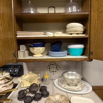 Sale Photo Thumbnail #37: Assorted kitchenware and dishware displayed on a countertop and inside a wooden cabinet, including a mini Yixing clay tea set, vintage Pyrex mixing bowls, colanders, and serving platters.