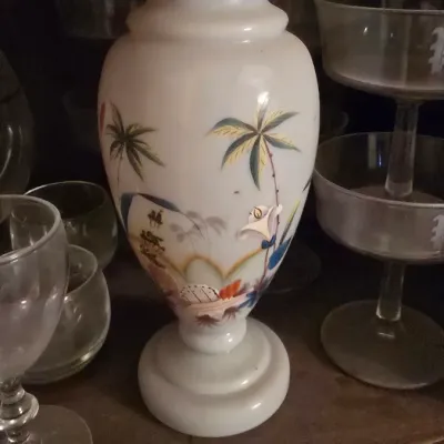 Sale Photo Thumbnail #61: Hand-painted opal glass vase featuring palm trees and a landscape scene, surrounded by assorted glassware.