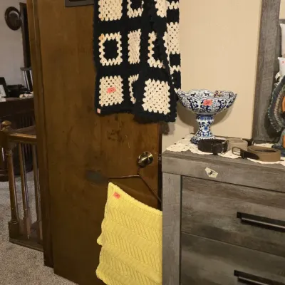 Sale Photo Thumbnail #14: Handmade black and white granny square crochet afghan blanket draped over a wooden door, shown alongside a yellow knit throw pillow.