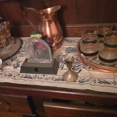 Sale Photo Thumbnail #64: Vintage barware and home decor collection, including mid-century gold-rimmed glassware on trays, a copper pitcher, a brass candlestick, and an etched glass display plaque.