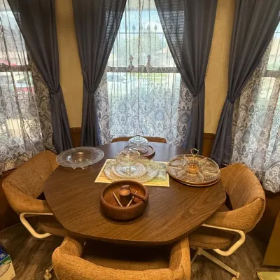 Sale Photo Thumbnail #35: Vintage 1970s wood grain laminate dining set featuring a rounded table and four upholstered swivel caster chairs, displayed with various glassware and wooden serving pieces.