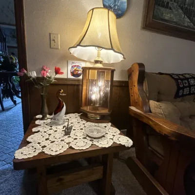 Sale Photo Thumbnail #54: Vintage illuminated glass and wood table lamp displayed on a rustic end table alongside decorative figurines, artificial flowers, and a crocheted lace runner.