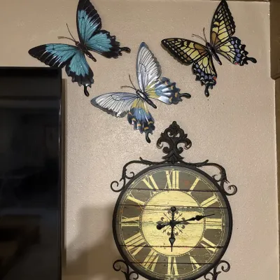 Sale Photo Thumbnail #51: Wrought-iron style wall clock with Roman numerals displayed below three decorative metal butterfly wall sculptures.